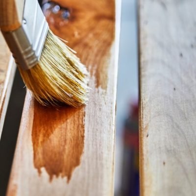 Man's hand holding a paint brush applying varnish to birch wood slats with shallow depth of field